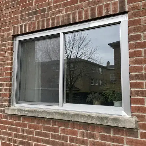 Aluminum-framed sliding window set in a red brick wall with a concrete sill