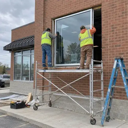 Two workers in hi-vis vests on rolling scaffold setting a large window into a