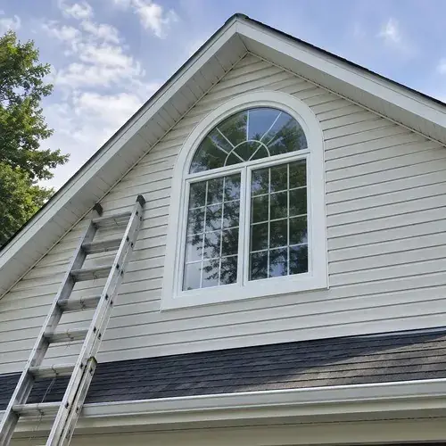 Arched-top white window with grilles installed in a vinyl-sided house gable