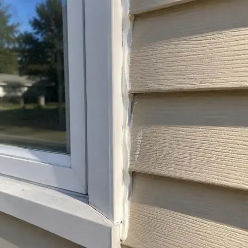 Close-up of white window frame corner with fresh caulk bead sealing the joint against