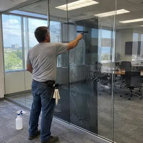 Man squeegees window film onto a large glass partition wall in a bright office