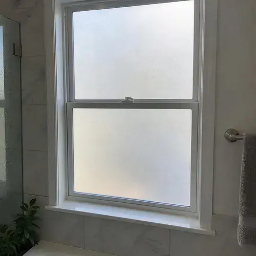 White double-hung bathroom window with frosted privacy film or glass beside tiled wall and