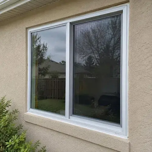 Completed two-panel slider window with white frame set in beige stucco wall of a
