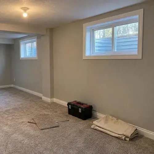 Finished basement room with small white sliding windows high on the wall