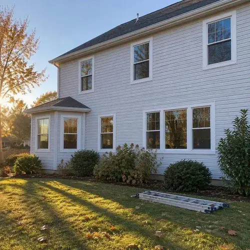 Two-storey home with light siding and multiple white-trimmed windows including a bay section