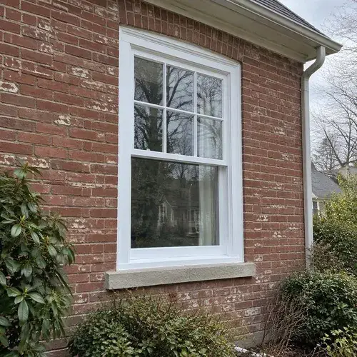 White double-hung window with grid pattern in a red brick house exterior with stone