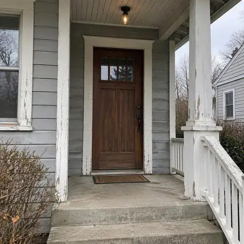 Stained wood craftsman-style entry door with small glass panes under a covered porch of